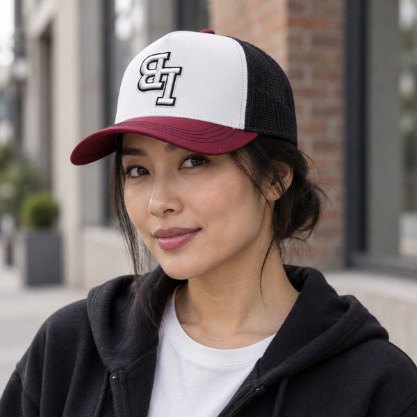 Woman wearing a Late Brake burgundy, white and black trucker hat with an embroidered LB monogram outdoors.