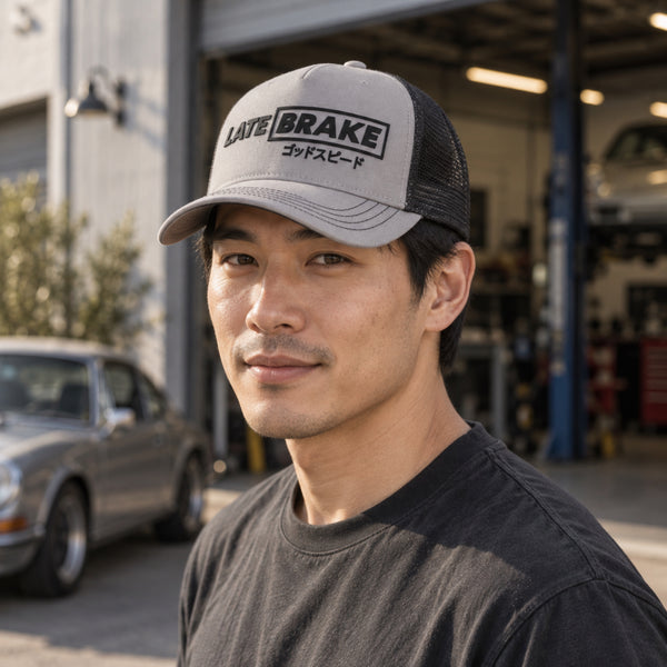 Man wearing a Late Brake grey and black mesh trucker hat with a black LATE BRAKE wordmark outdoors.