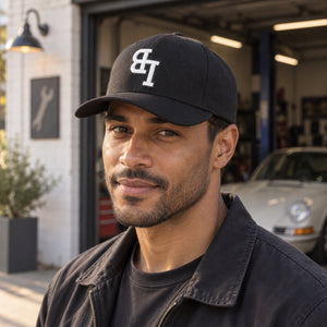 Man wearing a Late Brake black curved brim cap with a white embroidered LB monogram outdoors.