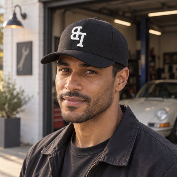 Man wearing a Late Brake black curved brim cap with a white embroidered LB monogram outdoors.