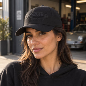 Woman wearing a Late Brake black curved brim cap with a tonal LATE BRAKE wordmark outdoors.