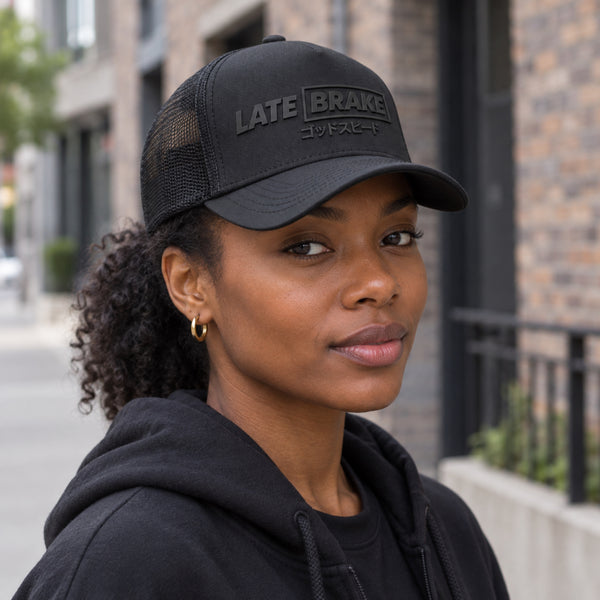 Woman wearing a Late Brake black mesh trucker hat with a tonal LATE BRAKE wordmark outdoors.