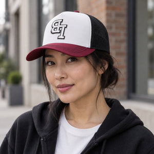 Woman wearing a Late Brake burgundy, white and black trucker hat with an embroidered LB monogram outdoors.