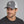 Man wearing a Late Brake grey and white mesh trucker hat with an embroidered LB monogram against a neutral studio background.