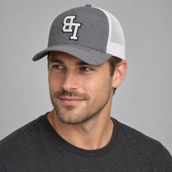 Man wearing a Late Brake grey and white mesh trucker hat with an embroidered LB monogram against a neutral studio background.