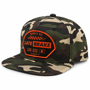 Late Brake woodland camo flat brim cap with an orange LATE BRAKE patch on a white background.