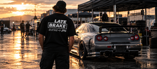 Late Brake JPN shirt beside a silver performance car at sunset